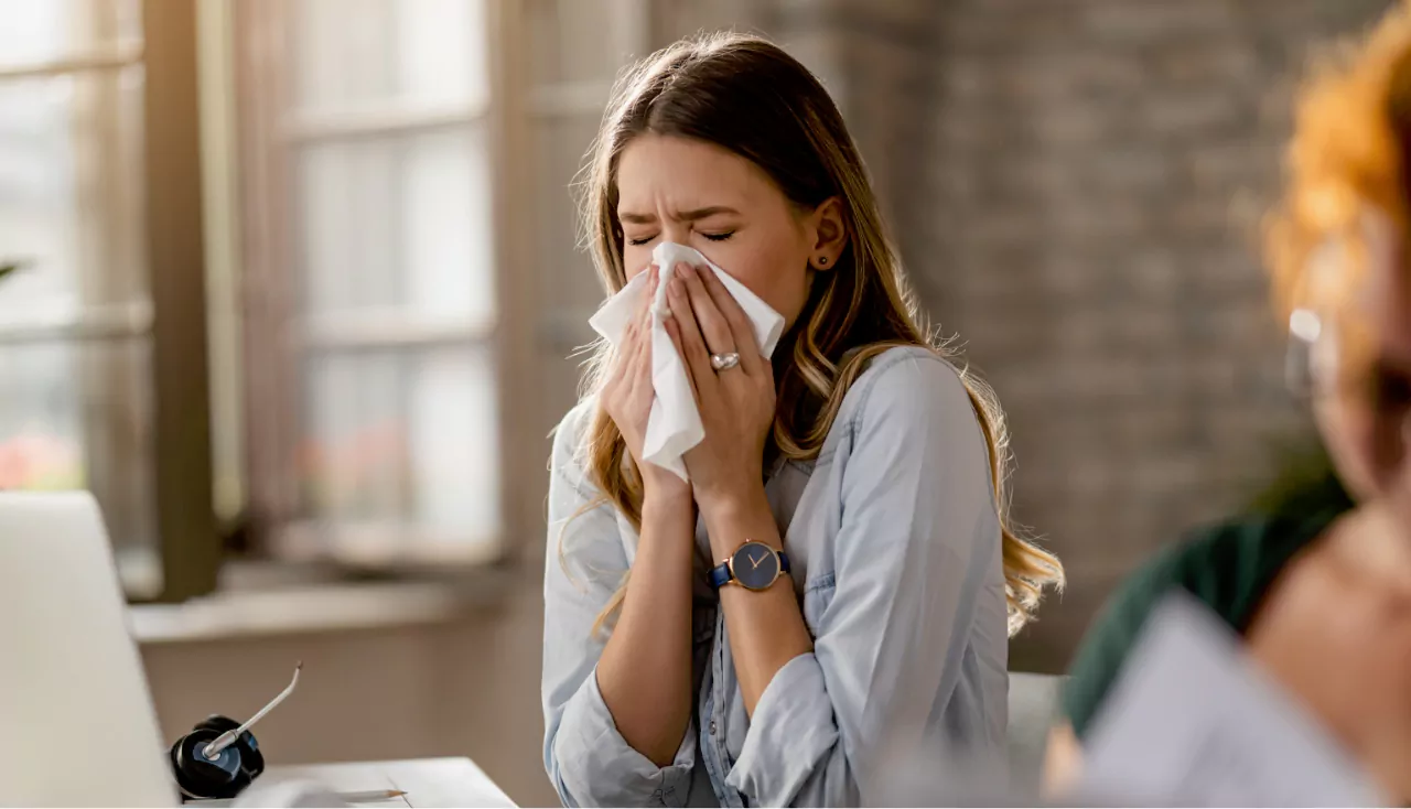 Young businesswoman using a tissue while sneezing in the office.